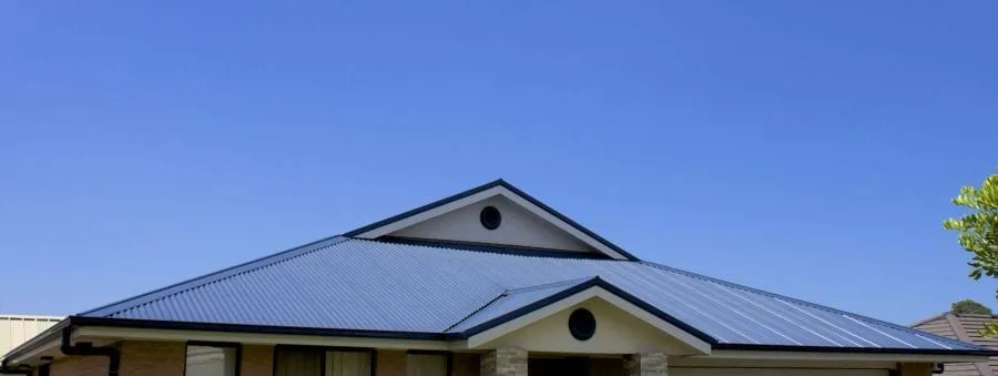 A freshly installed COLORBOND metal roof on a brick home under a clear blue sky